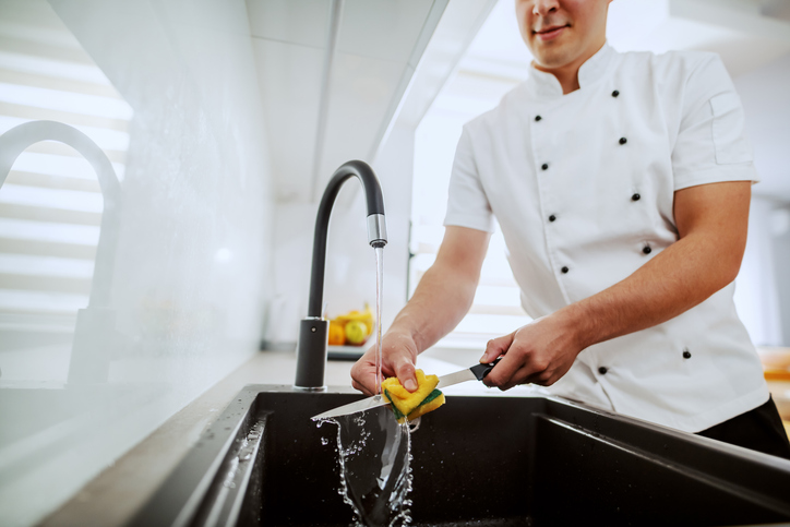 Male chef washes a kitchen knife in the sink