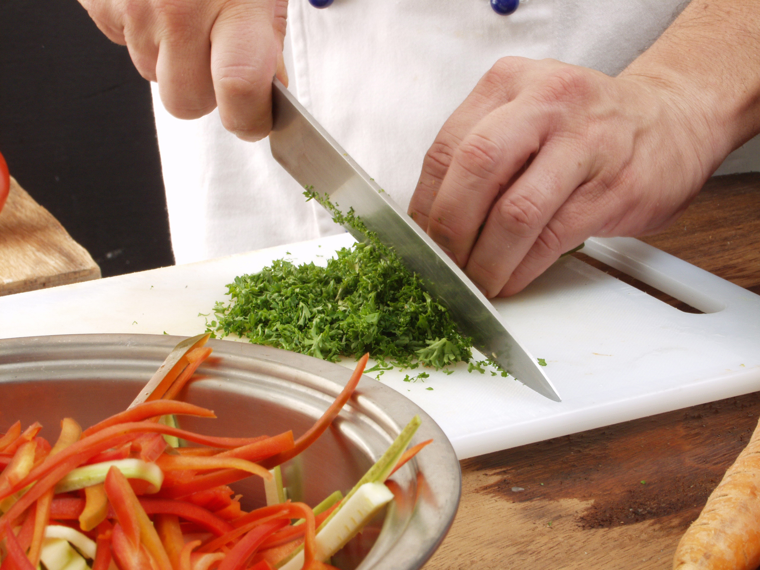 A chef chopping parsley using a large kitchen knife
