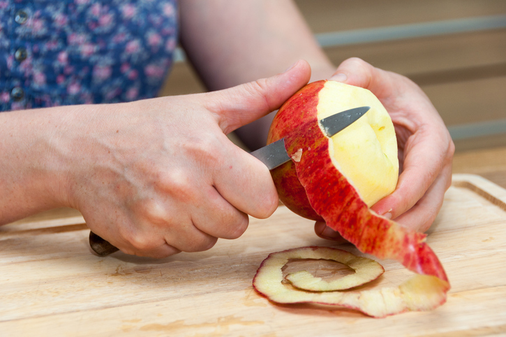 Hands peeling a cooking apple with a knife on a wooden board
